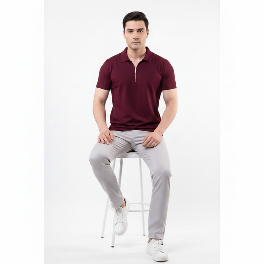 Man sitting on a stool wearing a maroon polo shirt and light gray pants against a white background